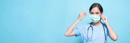 Portrait of young Asian beautiful nurse in blue uniform and wearing a surgical mask for protection...