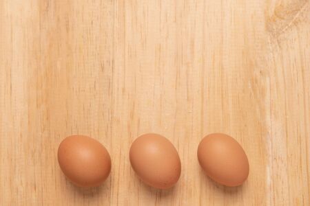 Three chicken egg on a light brown wooden background, Top view with copy space