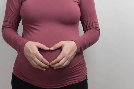 Close up of core body of pregnant woman wear red long sleeved t-shirt show her hand  symbolize the heart on her stomach, studio light portrait and copy space on white blackgroundの写真素材