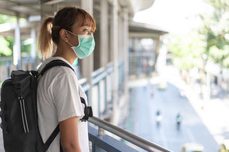 Asian woman with surgical face mask feel tired standing on skywalk after travel by skytrain, carrying backpack,  traveling to the city, social distancing, coronavirus, COVID19の写真素材
