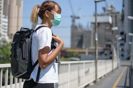Asian woman with surgical face mask, carrying backpack,  traveling to the city standing on overpass...