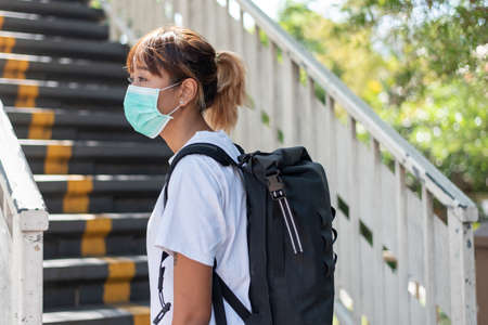 Asian woman with surgical face mask, carrying backpack,  traveling to the city standing on overpass bridge stairs, social distancing, coronavirus, COVID19の写真素材