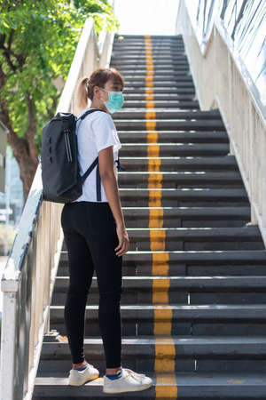 Asian woman with surgical face mask, carrying backpack,  traveling to the city standing on overpass bridge stairs, social distancing, coronavirus, COVID19の写真素材