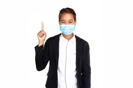 Asian businesswoman wearing surgical face mask in black suit jacket, looking at camera and pointing finger up, studio lighting isolated on white background, coronavirus, COVID19 conceptの写真素材