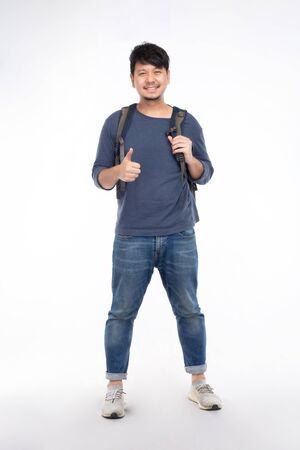 Smiling Asian man with long-sleeved T-shirts and blue jeans, shoulder backpack and show hand thumps up, isolated on white background, traveling conceptの写真素材