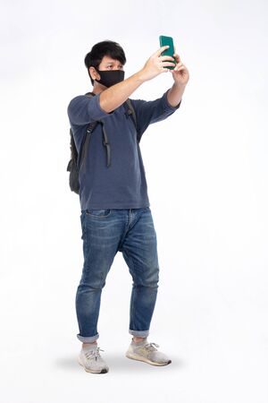 Asian man with black mask wear long-sleeved T-shirts, blue jeans, shoulder backpack and holding smartphone to find phone signal, isolated on white background, traveling conceptの写真素材