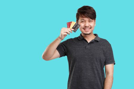 Smiling Asian man holding credit card, look at camera, studio light portrait isolated on blue backgroundの写真素材