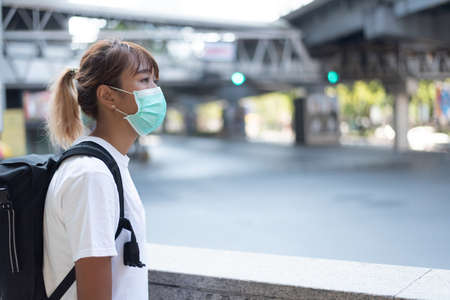 Asian woman with surgical face mask, carrying backpack,  traveling to the city standing on overpass...