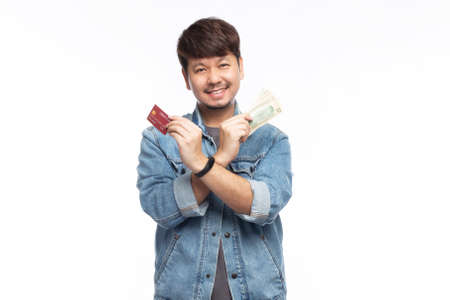 Happy Asian man in smiling face wear blue jeans jacket cross hands holding credit card and dollar...