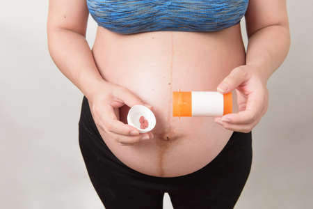 Close up the belly of pregnant woman her hand holding and show the bottle of vitamin and pill, isolated on white background, pregnancy conceptの写真素材