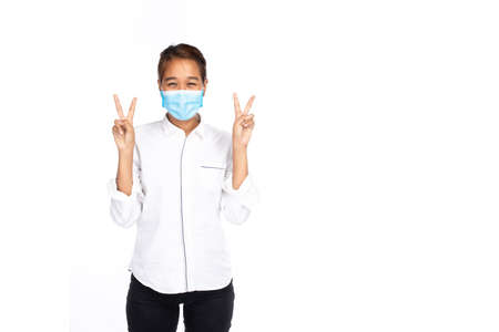 Happy Asian woman in white shirt wear face mask show two hands and raise two fingers up or victory...