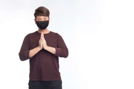 Asian man wear black protection face mask and greeting by Thai traditional respect, Sawatdee, new normal greeting, isolated on white backgroundの写真素材