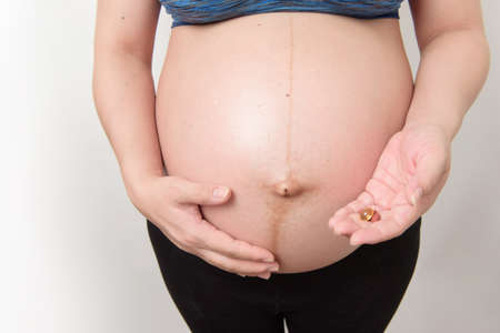 Close up the belly of pregnant woman her hand holding and show the vitamin and pill, isolated on...