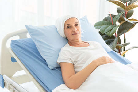 Side view of senior breast cancer patient wearing a headscarf laying in bed and praying in the...