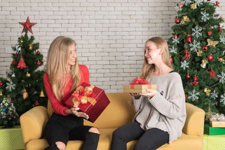 Two young women sitting on sofa holding gift box with happy expression In a room decorated for Christmasの写真素材