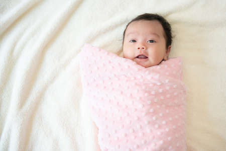 Top view of a cute Asian baby girl wrapped up in bedの写真素材