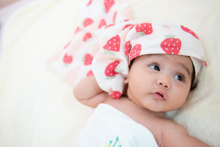 Cute Asian baby girl with a towel on her head lying on the bed after bathingの写真素材