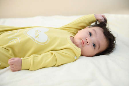 Side view portrait of cute little Asian baby lying on the white bed sheet, look at the camera