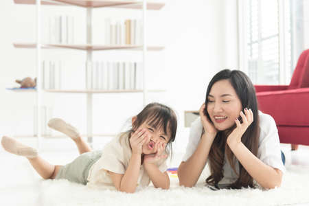 Happiness Asian young mother and little cute daughter lying on bed in the house using labtop for entertain, family joyful together in the house on holidayの写真素材