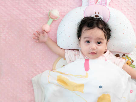 Top view of a cute little asian baby girl wrapped in a blanket lying on the bed, looking at cameraの写真素材