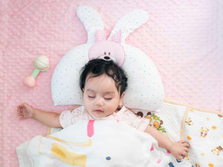 Top view of a cute little asian baby girl wrapped in a blanket sleeping on the bedの写真素材
