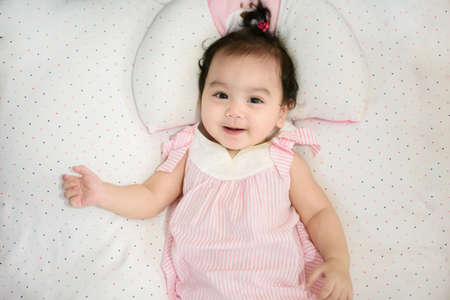 Top view of happy Asian baby girl lying on the bed, smiling and cheerful face, looking at the cameraの写真素材