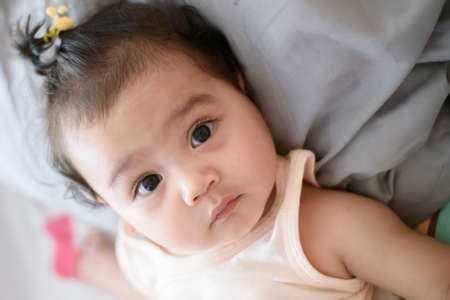 Portrait of cute little Asian baby girl lying on the bed and looking at the camera