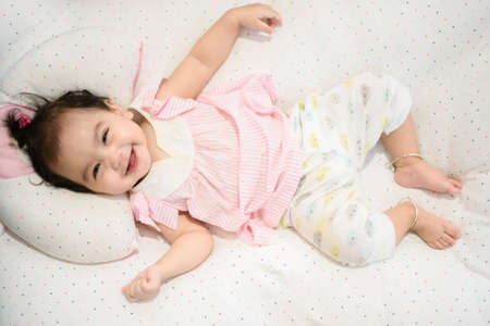 Top view of a cute happy Asian baby girl lying on the bed, smiling and cheerful face, looking at the cameraの写真素材