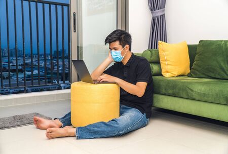 An asian men is working from home during Coronavirus or Covid-19 quarantine, coronavirus covid 19 infected patient in coronavirus covid 19 quarantine room using computerの写真素材