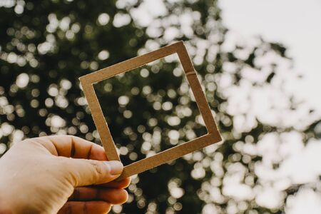 Hand holding blank paper frame with nature bokeh background. Text concept.