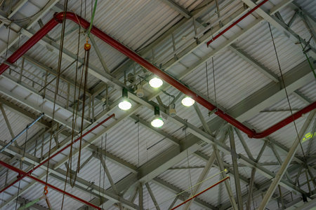 The steel construction roof of a sports hall and the spot lights on this roof. Wide shot of industrial hall empty and clean. Empty factory interior or storehouse. Background and industrial conceptの写真素材