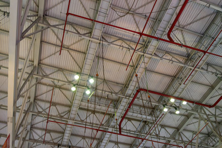The steel construction roof of a sports hall and the spot lights on this roof. Wide shot of industrial hall empty and clean. Empty factory interior or storehouse. Background and industrial conceptの写真素材