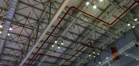 The steel construction roof of a sports hall and the spot lights on this roof. Wide shot of industrial hall empty and clean. Empty factory interior or storehouse. Background and industrial conceptの写真素材