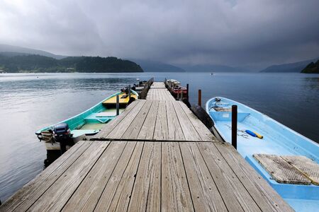 A wooden jetty with boats at Ashi Lake on a gloomy day.の素材