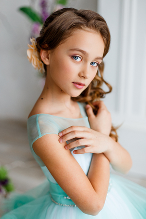 young girl with blue eyes, make up and hairstyle in lush turquoise dress in studio with flower decorationの写真素材