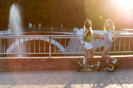 Happy girls riding on hover boards or gyroscooters outdoors at sunset in summer. Active life conceptの写真素材