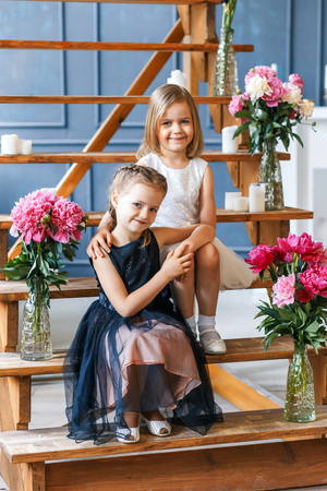 Two cute little girls with peonies. Two beautiful friends having fun, hugging and smilingの写真素材