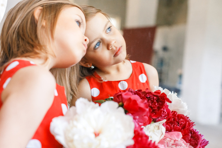 Two cute little girls with peonies. Two beautiful friends having fun, hugging and smilingの写真素材