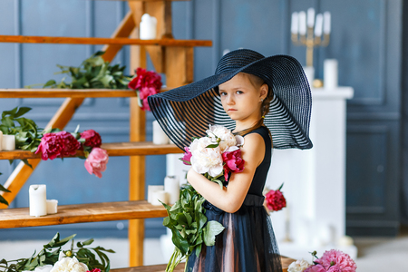 Cute little girl in big black hat with peonies in studioの写真素材