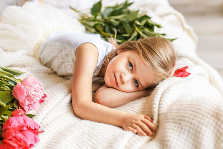Cute little girl with peonies in studio lying on the bed among peoniesの写真素材
