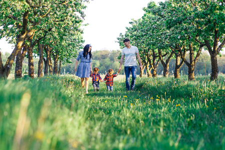 Happy young family spending time together outside in green nature. Parents playing with twins. Family of four walkngの写真素材