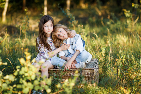 a cute little boy and a girl sitting on a basket outside at sunset an having funの写真素材