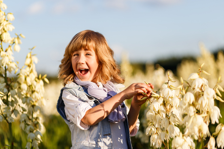 A portrait of a cute little boy with blue eyes and long blond hair outside in the field of flowers having funの写真素材