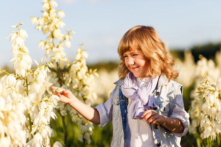 A portrait of a cute little boy with blue eyes and long blond hair outside in the field of flowers having funの写真素材
