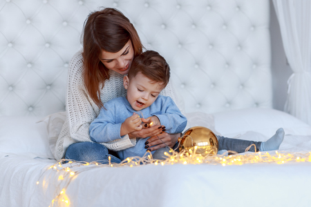 A boy with his mom in front of the christmas tree with candles and gifts. New year's eve. Cozy holiday at the fir-tree. love, happiness and big family conceptの写真素材