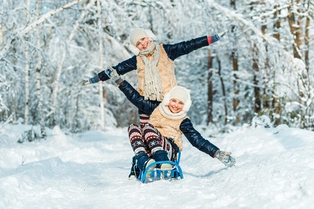 Beautiful teenage girls twins sisters riding sledge and having fun outside in a wood with snow ....