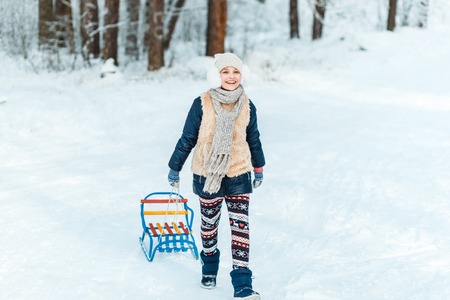 A girl with sledge. Beautiful teenage girl having fun outside in a wood with snow in winter. active life conseptの写真素材