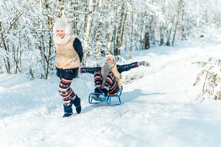 Beautiful teenage girls twins sisters riding sledge and having fun outside in a wood with snow . Friendship conseptの写真素材