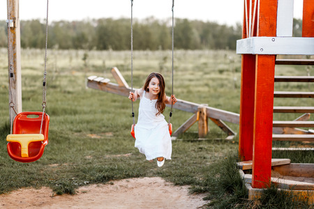 Little girl is swinging at a playground when the sun is setting. Happiness and family conceptの写真素材
