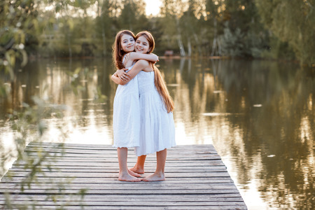 Beautiful girls friends with long brunette hair ans blue eyes having fun on the pier with beautiful wiev near the water at the sunsetの写真素材